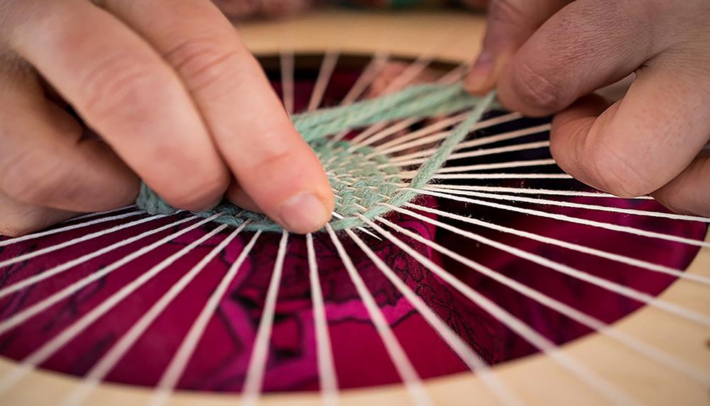 Close up image of hands weaving on a circular frame